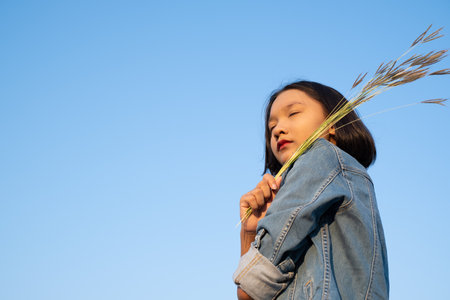 Young asian girl wear Jetket Jean hold grass flower .Blue sky background.