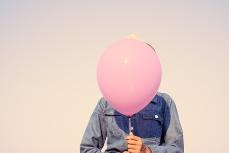 Asian young girl wear hat and Jean hold pink balloon with blue sky background.Vintage color.