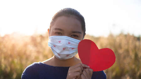 Girl wera heart mask and hold red paper heart with grass background.の写真素材