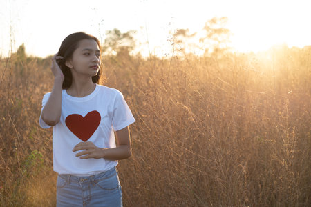 Portrait young griel wear white shirt and red heart at meadow with rim ligth time.の写真素材