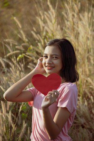 Young Asian girl hold red heart paper at meadow background.の写真素材
