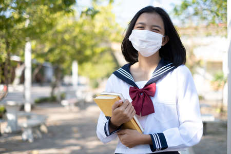 Asian student hold book and wear mask in school uniform.の写真素材