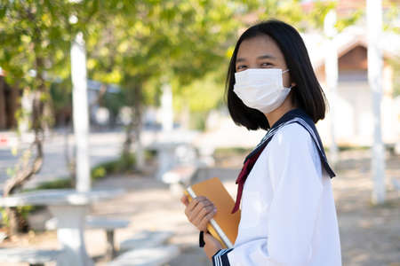 Asian student hold book and wear mask in school uniform.の写真素材