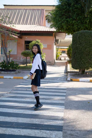 Smiling Asian young girl wear uniform with backpack walking at crossing road at school.の写真素材