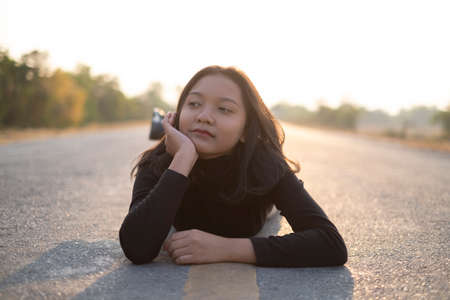 Portrait beautiful girl lay down on the long road, looking camera, sunset time.の写真素材