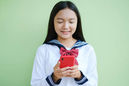 Happy young girl using smartphone on green background,Asian girl,School girl.の写真素材