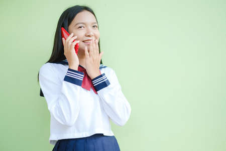 Happy young girl using smartphone on green background,Asian girl,School girl.の写真素材