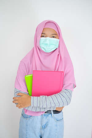 Student young girl wear pink hijab and mask hold books on white background.の写真素材