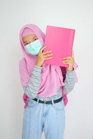 Student young girl wear pink hijab and mask hold books on white background.の写真素材