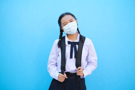 School girl wear mask with backpack on blue background.