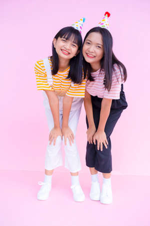 Two happy young girl standing on pink background.
