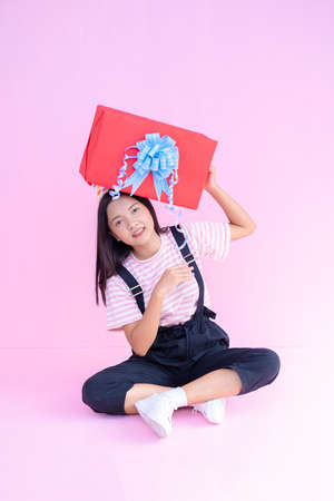 Happy young girl hold red gift box sitting on pink background .の写真素材