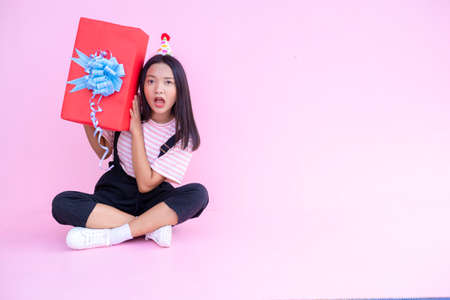 Happy young girl hold red gift box sitting on pink background .の写真素材