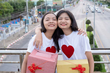 Two happy girls with gift boxes standing with city background.の写真素材