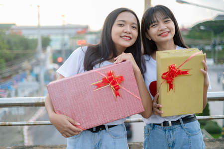 Two happy girls with gift boxes standing with city background.の写真素材