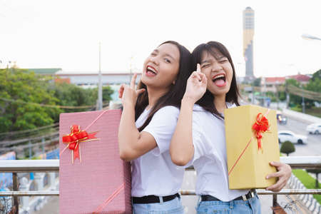 Two happy girls with gift boxes standing with city background.の写真素材