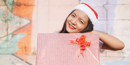 A beautiful girl wear Christmas hat hold present on colorful background.の写真素材