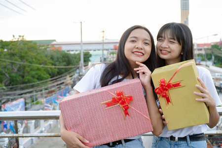 Two happy girls with gift boxes standing with city background.の写真素材