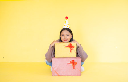 Happy young girl with gift box , Asian girl wear brow sweater on yellow background.の写真素材