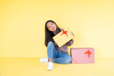 Happy young girl with gift box , Asian girl wear brow sweater on yellow background.の写真素材