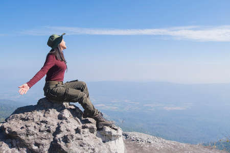 Tourist girl siting on the stone at the mountain, wear hat and looking panoramic view at Pha Mak Dook Phukradung National park at Thailand.の写真素材
