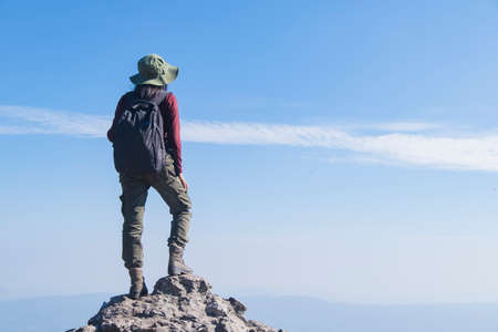 Tourist girl with backpack standing on the stone at the mountain, wear hat and looking panoramic view at Pha Mak Dook Phukradung National park at Thailand.の写真素材