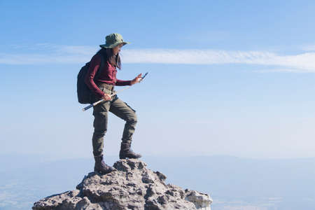 Tourist girl with backpack standing on the stone at the mountain, wear hat and looking panoramic view at Pha Mak Dook Phukradung National park at Thailand.の写真素材