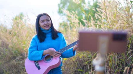 Happy young girl playing guitar and make vdo at the meadow.の写真素材