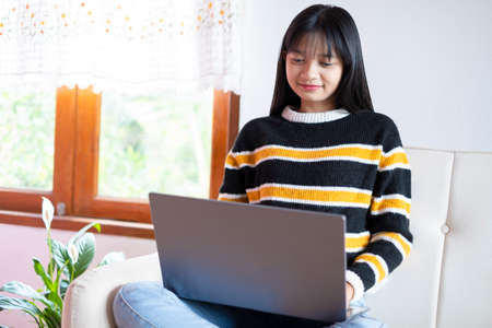 Happy young girl use computer laptop, sitting on sofa at home.の写真素材