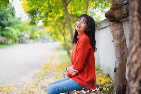 Happy young girl wear orange sweater under the tree and  yellow flower.の写真素材