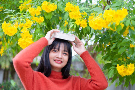 Happy girl wear orange sweater hold book on yellow flower background.の写真素材