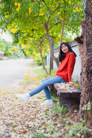 Happy young girl wear orange sweater under the tree and  yellow flower.の写真素材