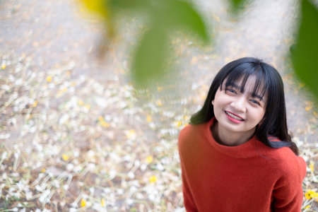 Happy young girl wear orange sweater under the tree and  yellow flower.の写真素材