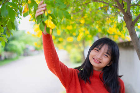 Happy young girl wear orange sweater under the tree and  yellow flower.の写真素材
