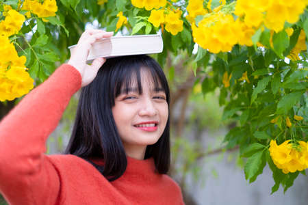 Happy girl wear orange sweater hold book on yellow flower background.の写真素材