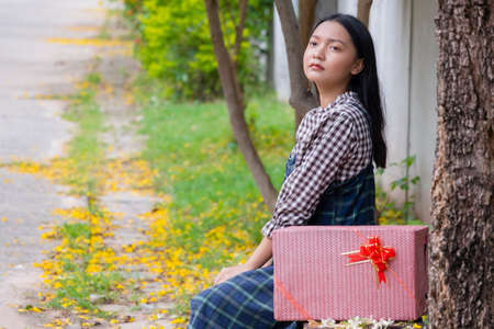 Beautiful young girl sitting under the tree with gift box.の写真素材