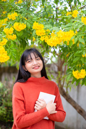 Happy girl wear orange sweater hold book on yellow flower background.の写真素材