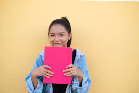 Happy student young girl with pink book on brown background.の写真素材