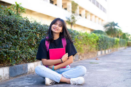Student young girl with pink backpack sitting at on foor with school background.