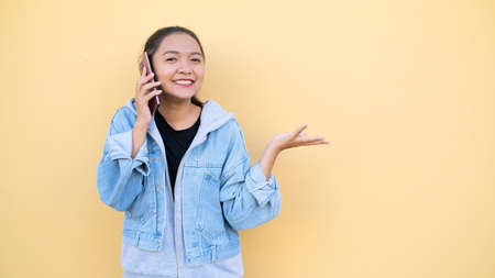 Portrait beautiful young girl wear jacket jean talking with mobile on orange bcakground,Asian girl.の写真素材