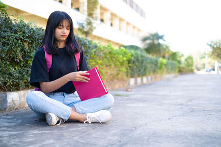 Student young girl with pink backpack sitting at on foor with school background.の写真素材