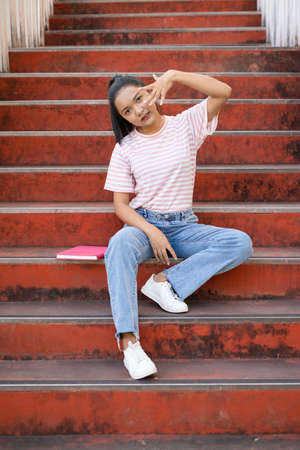 School girl  wear pink shirt and jean holding and holding pink book on stairs.の写真素材