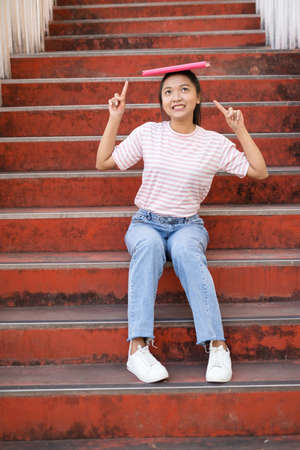 School girl  wear pink shirt and jean holding and holding pink book on stairs.の写真素材