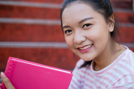 Smile young girl hold pink book sitting at school,Asian girl.の写真素材