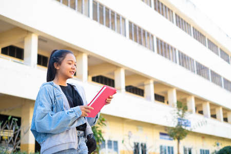 Smile girl hold pink book standing on building background,Back to school.の写真素材