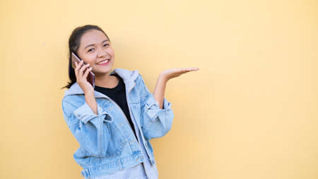 Portrait beautiful young girl wear jacket jean talking with mobile on orange bcakground,Asian girl.の写真素材