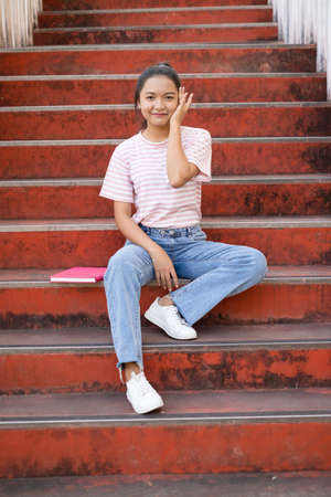 School girl  wear pink shirt and jean holding and holding pink book on stairs.の写真素材