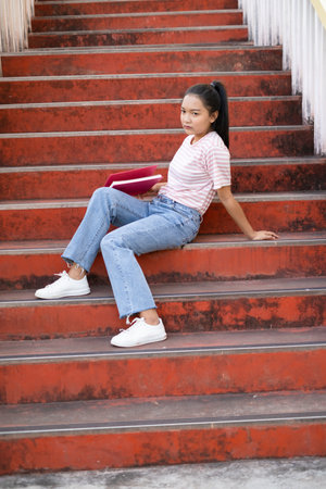 School girl  wear pink shirt and jean holding and holding pink book on stairs.の写真素材