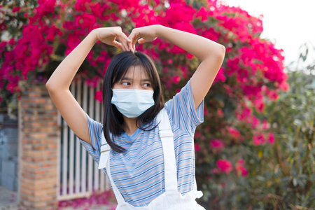 Portrait Young Asian girl wear mask outdoor, beautiful flower background.