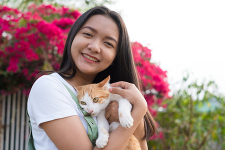 Portrait Young Asian girl with a cat outdoor, beautiful flower background.の写真素材